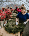 Person making a wreath in a greenhouse with floral arrangements around