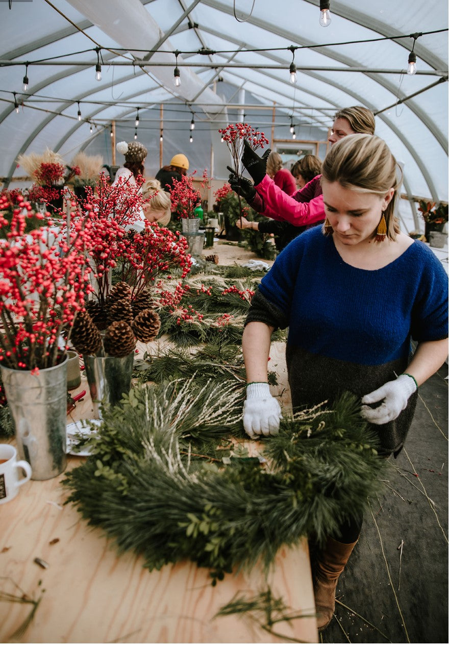 Person making a wreath in a greenhouse with floral arrangements around